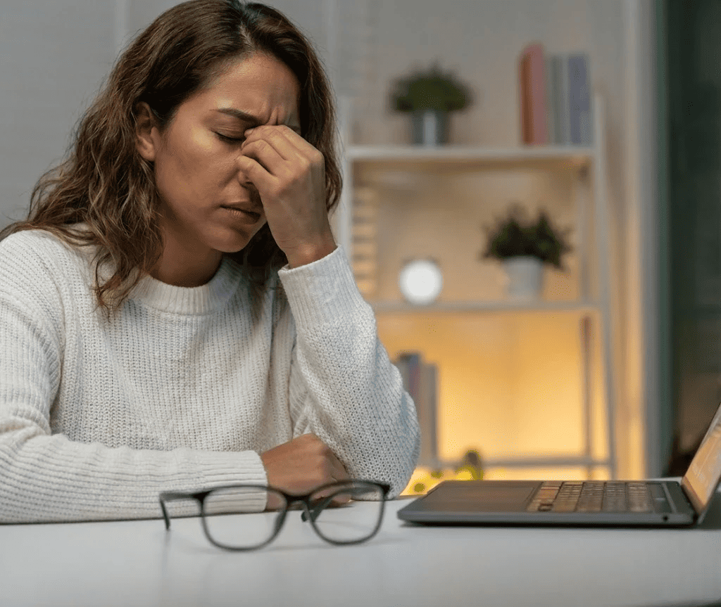 Mujer frotándose los ojos frente a una computadora por fatiga visual